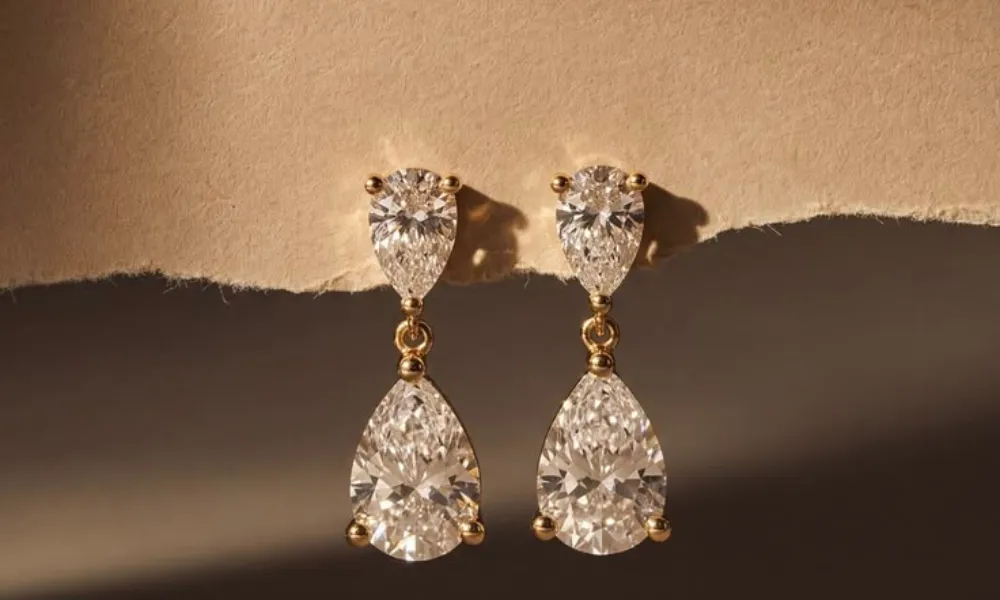 Luxury Fine Jewelry featured in a close-up photo of pear-cut diamond drop earrings set in gold, displayed against a textured paper background. 