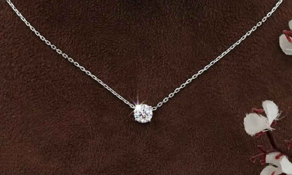 luxury diamond necklaces featured in a detailed view of a delicate silver chain supporting a sparkling round-cut solitary diamond pendant set against a dark brown fabric backdrop. 