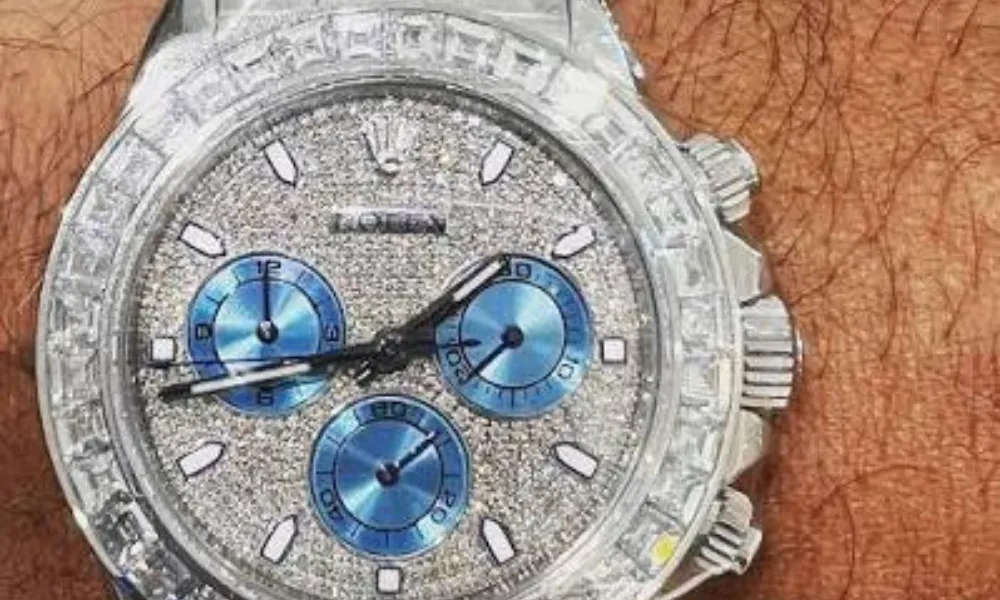 Luxury of Time by Diamonds International featured in a close-up photo of a diamond-encrusted Rolex Daytona watch with a pavé dial, baguette diamond bezel, and blue sub-dials. 