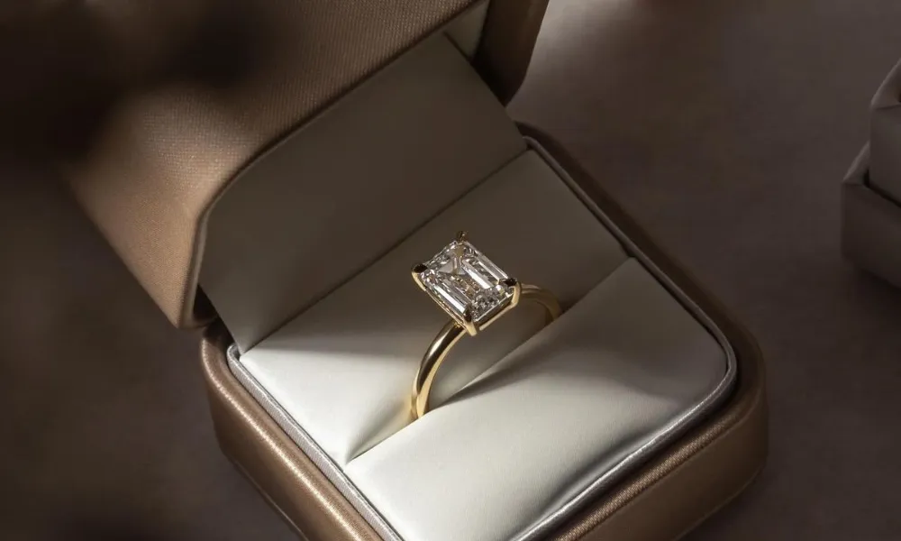 Luxury Engagement Ring Box featured in a close-up photo of an emerald-cut diamond solitaire ring set on a gold band inside an open satin-lined gold presentation box.