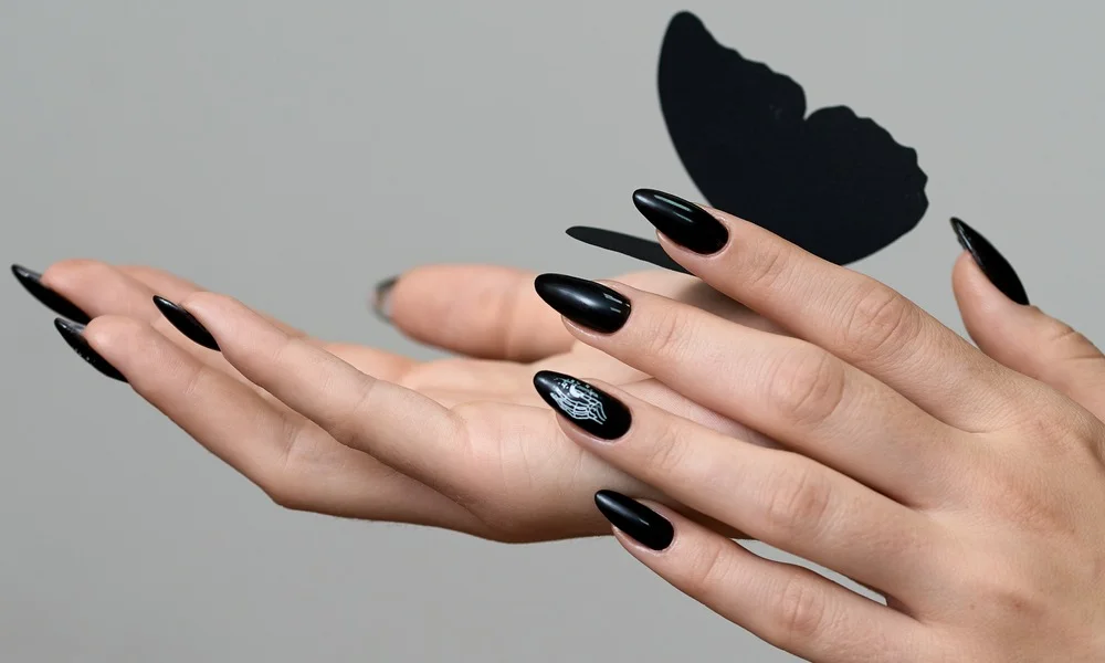 Elegant hands display long glossy black stiletto nails against a gray background, with a black butterfly silhouette above, creating a dramatic, fashion-forward mood.
