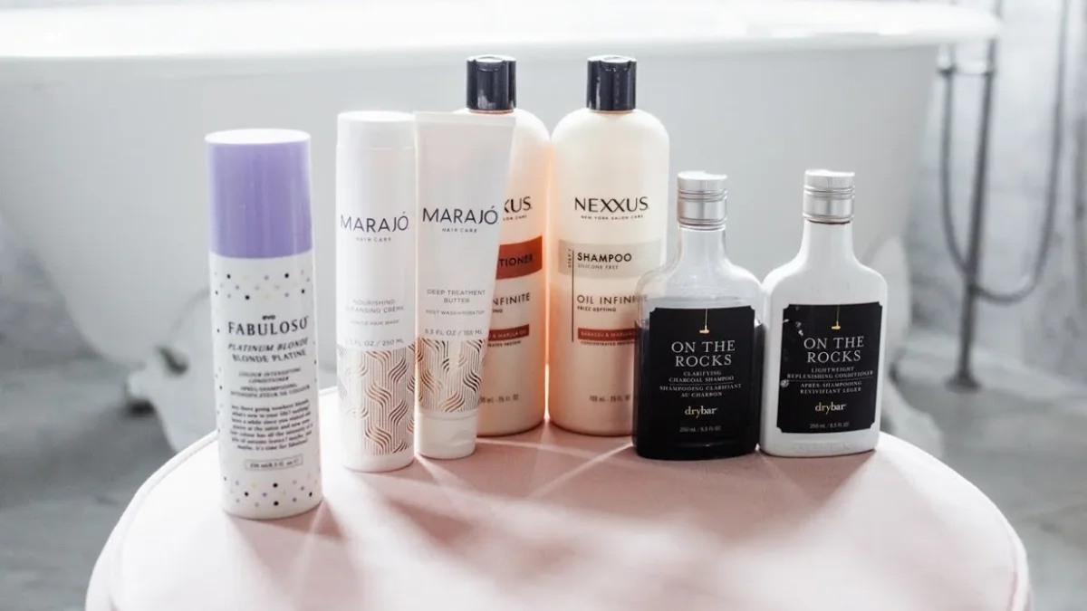 Haircare products—sprays, shampoo, and conditioner from brands including Fabuloso, Marajó, Nexxus, and On the Rocks—neatly arranged on a pale pink stool in a bright, minimalist bathroom.