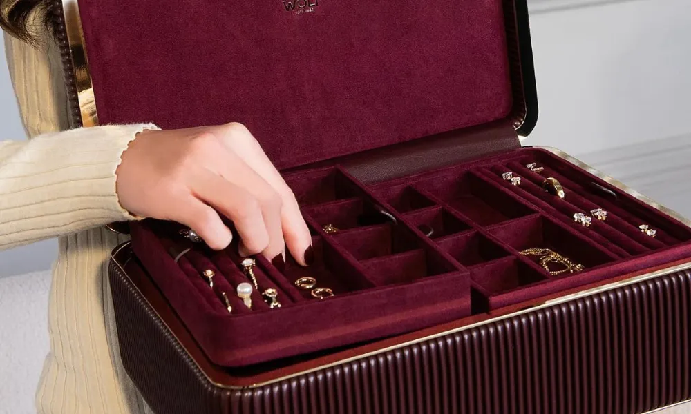 Luxury Jewelry Case featured in a photo of a woman organizing rings and accessories inside an open maroon WOLF jewelry trunk. 