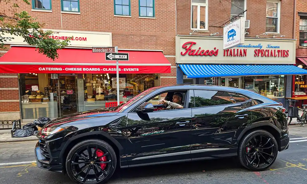 Black Lamborghini Urus luxury SUV driving past a New York storefront