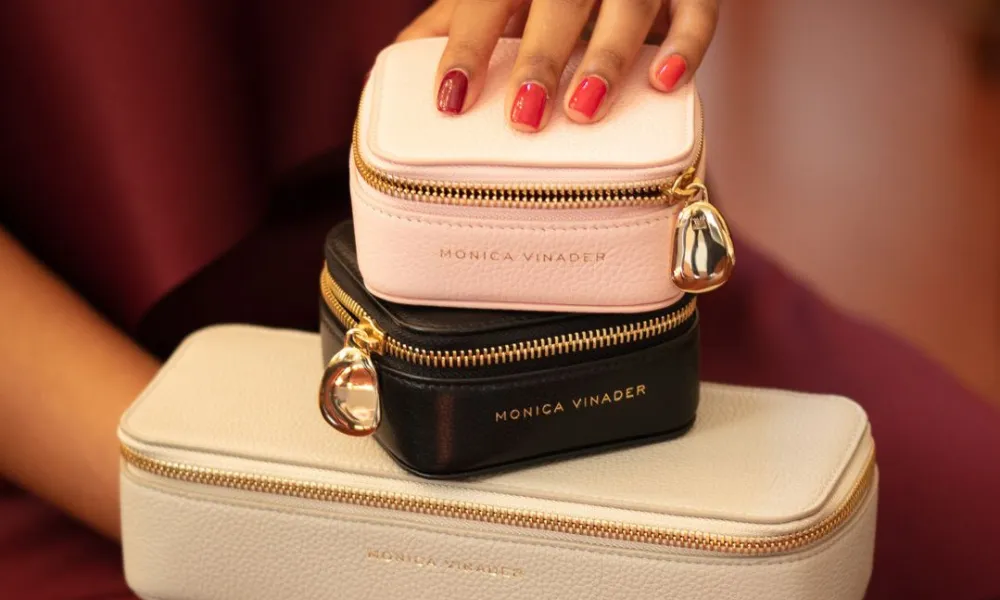 Luxury Jewelry Case featured in a photo of stacked Monica Vinader leather travel jewelry cases held by a woman wearing gold rings. 