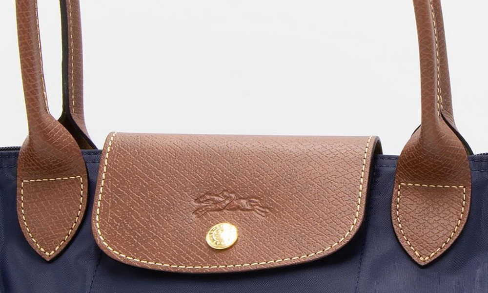 Close-up of a foldable tote bag with leather handles and flap closure.