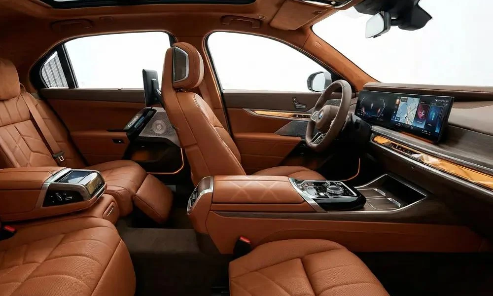 Spacious luxury car interior featuring tan leather executive seating, digital widescreen displays, and ambient lighting