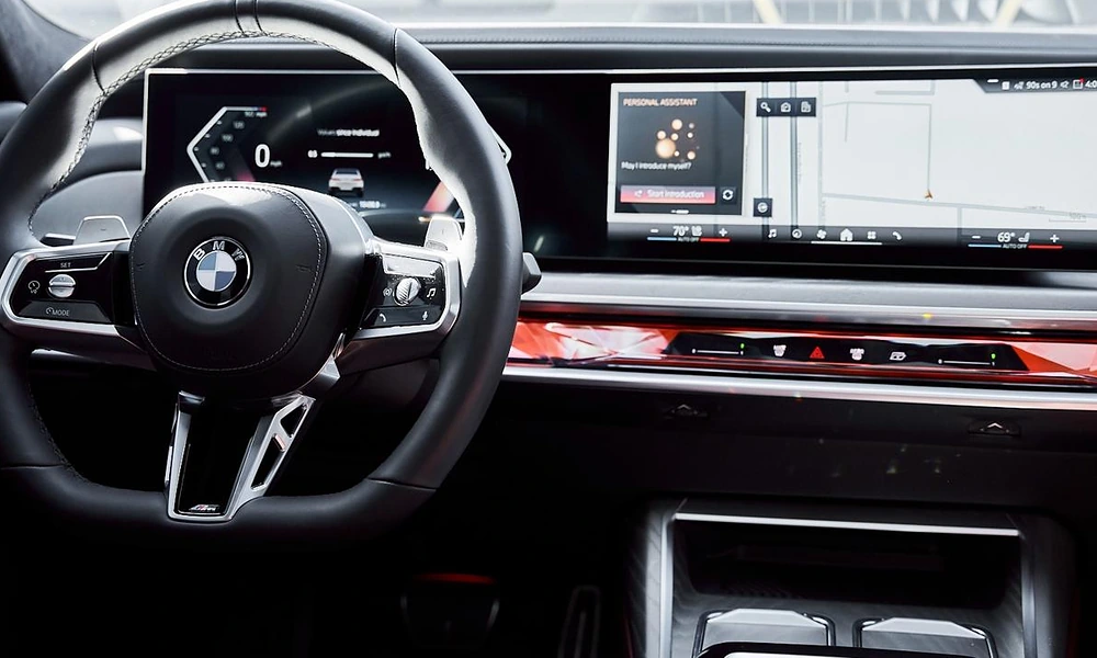 Driver perspective showing a leather steering wheel in front of a wide curved digital navigation and infotainment screen
