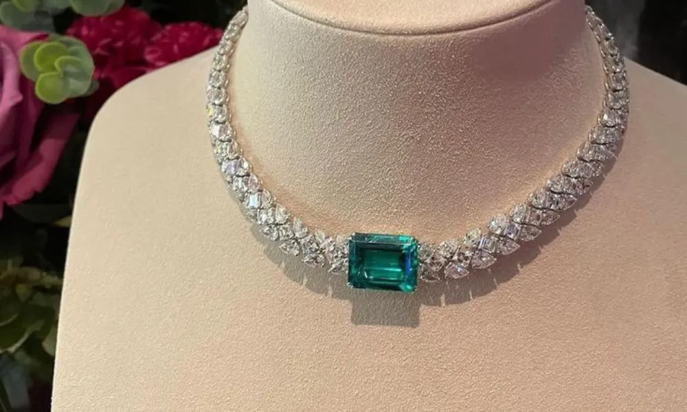 luxury diamond necklaces featured in a detailed view of a double-row diamond collar necklace centered with a prominent emerald-cut green gemstone on a beige display mannequin. 