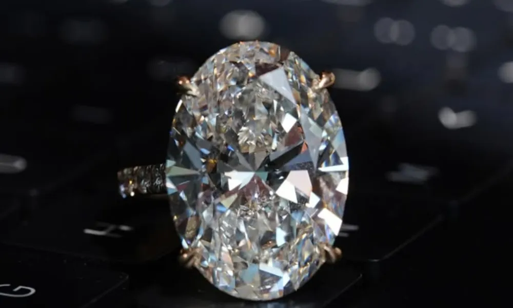 Luxury Diamonds featured in a close-up photo of a large oval-cut solitaire diamond engagement ring set on a pavé band resting on a dark keyboard background.