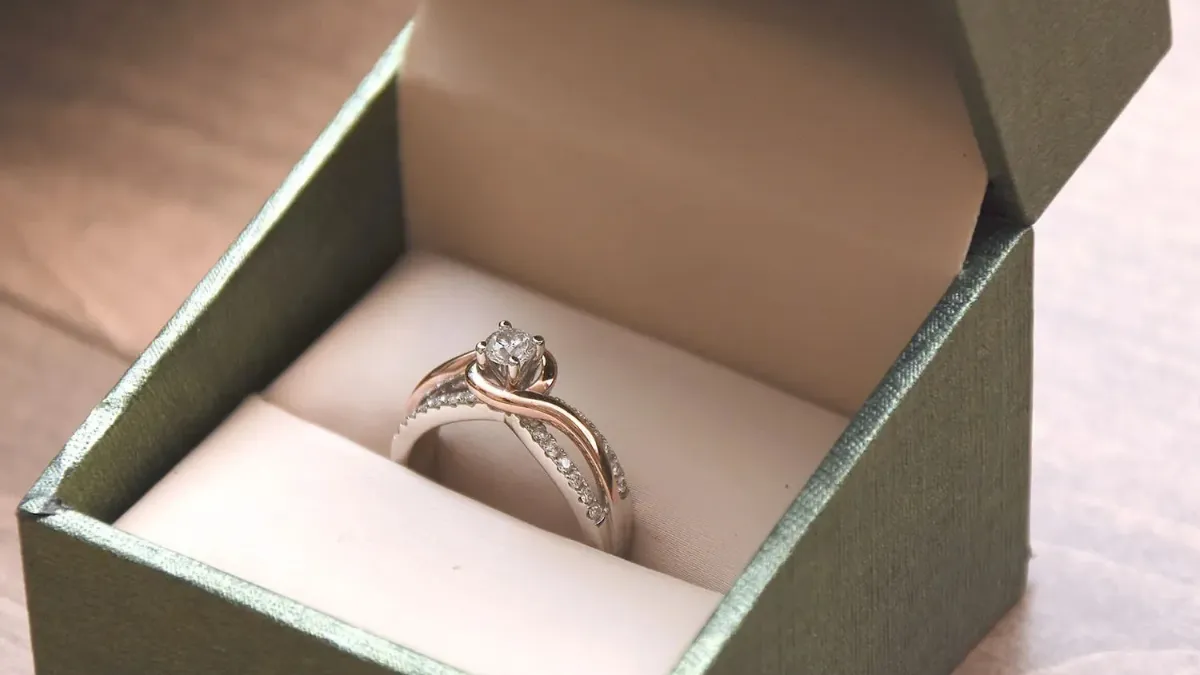Luxury Engagement Ring Box featured in a close-up photo of a round solitaire diamond engagement ring with a two-tone twisted bypass band inside an open dark green jewelry box.