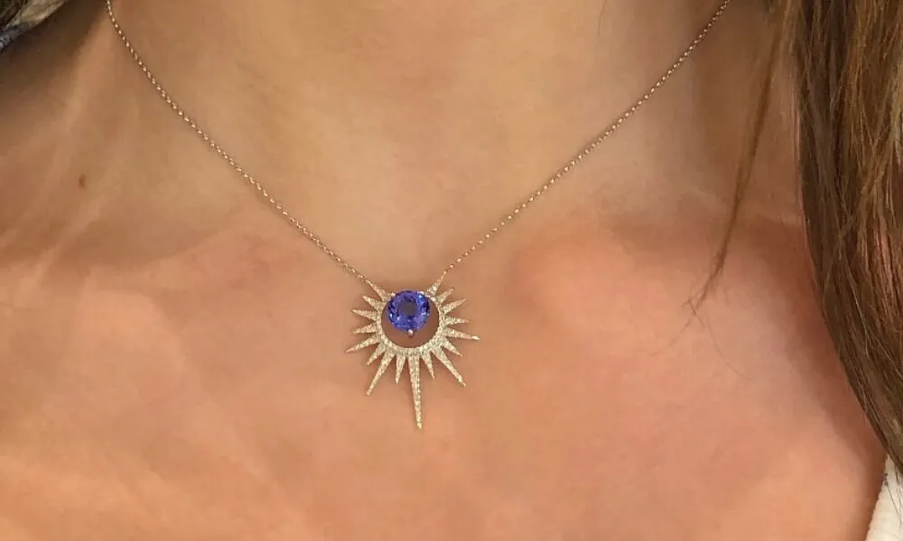Luxury of Time by Diamonds International highlighted in a close-up view of a gold chain necklace with a radiant-cut diamond pendant set in a starburst pavé frame worn around a neck. 