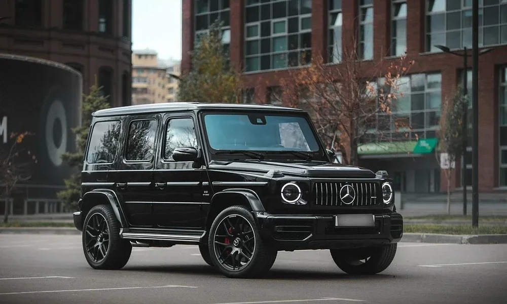 Glossy black Mercedes-AMG G 63 parked on an urban street near brick buildings