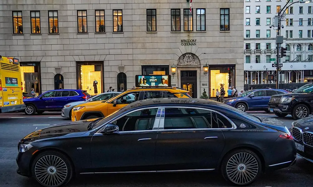 Black Mercedes-Maybach executive sedan driving past storefronts on a busy New York street