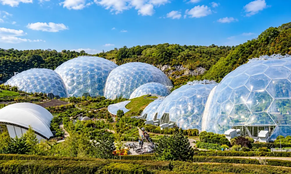 Eden Project biomes in Cornwall, England, with large transparent domes and landscaped gardens on a green hillside under a blue sky