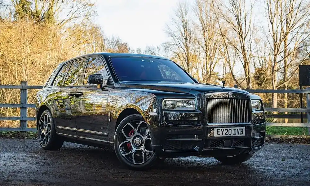 Glossy black Rolls-Royce Cullinan luxury SUV parked along a country estate road