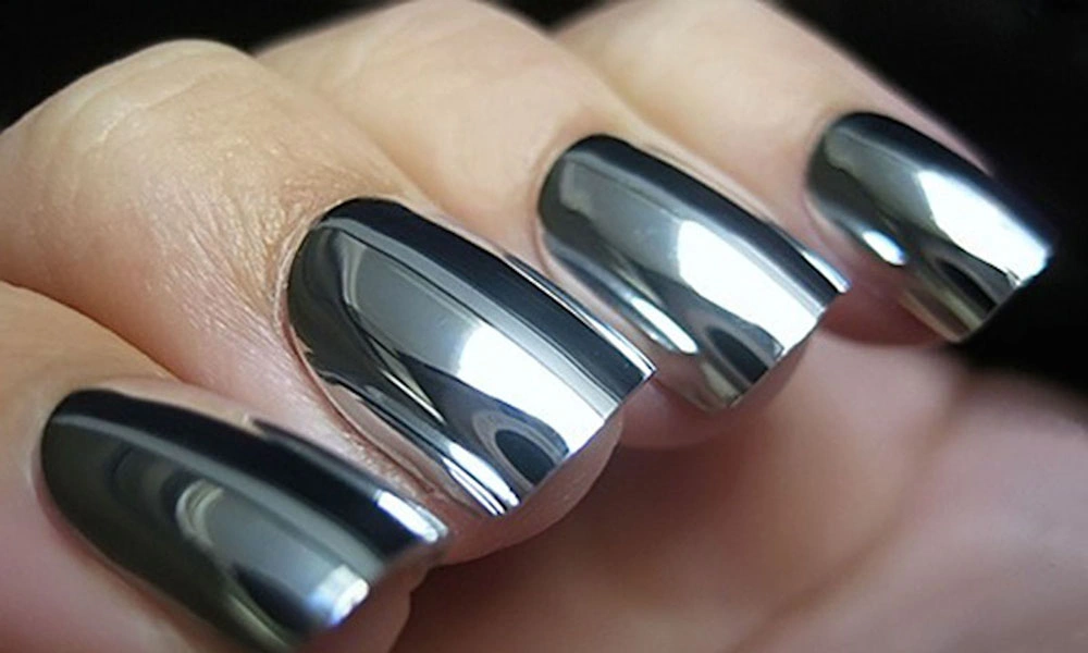 Close-up of a hand with long, sculpted nails coated in mirror-like chrome polish, reflecting light in silver and blue tones; sleek, futuristic glamour.