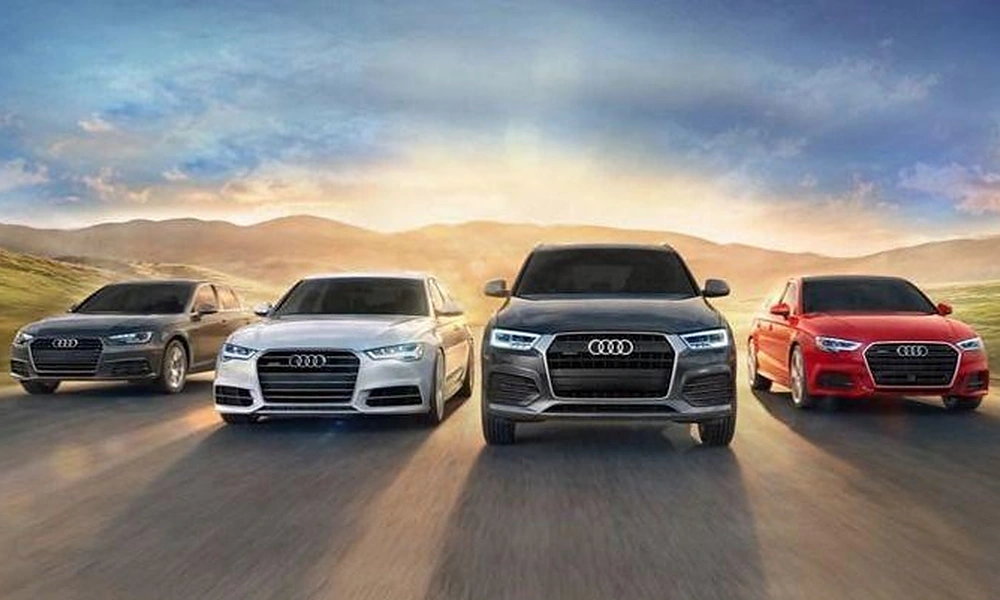 Lineup of four executive sedans and crossover SUVs driving along a scenic road at sunset