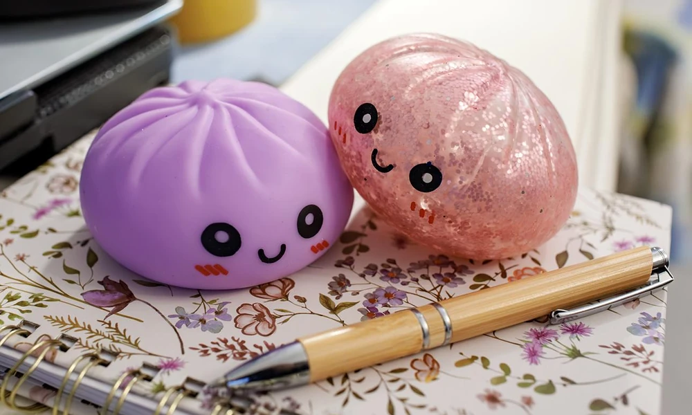 Two cute smiling dumpling NeeDoh squishy toys sitting on a floral notebook next to a wooden pen