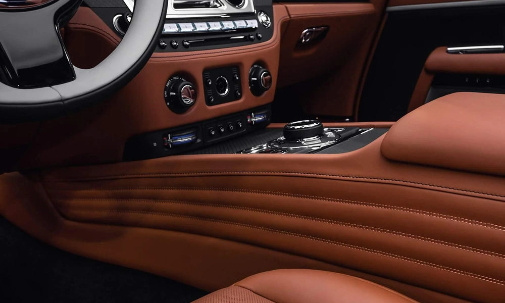 Close-up view of stitched cognac brown leather trim and metallic climate dials on a vehicle center console
